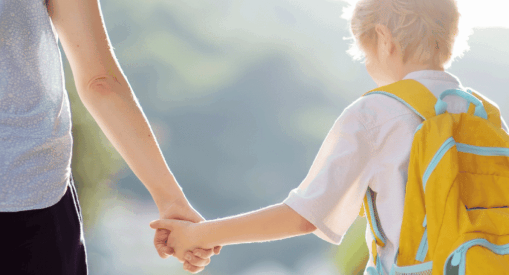 child with backpack on holds adult hand