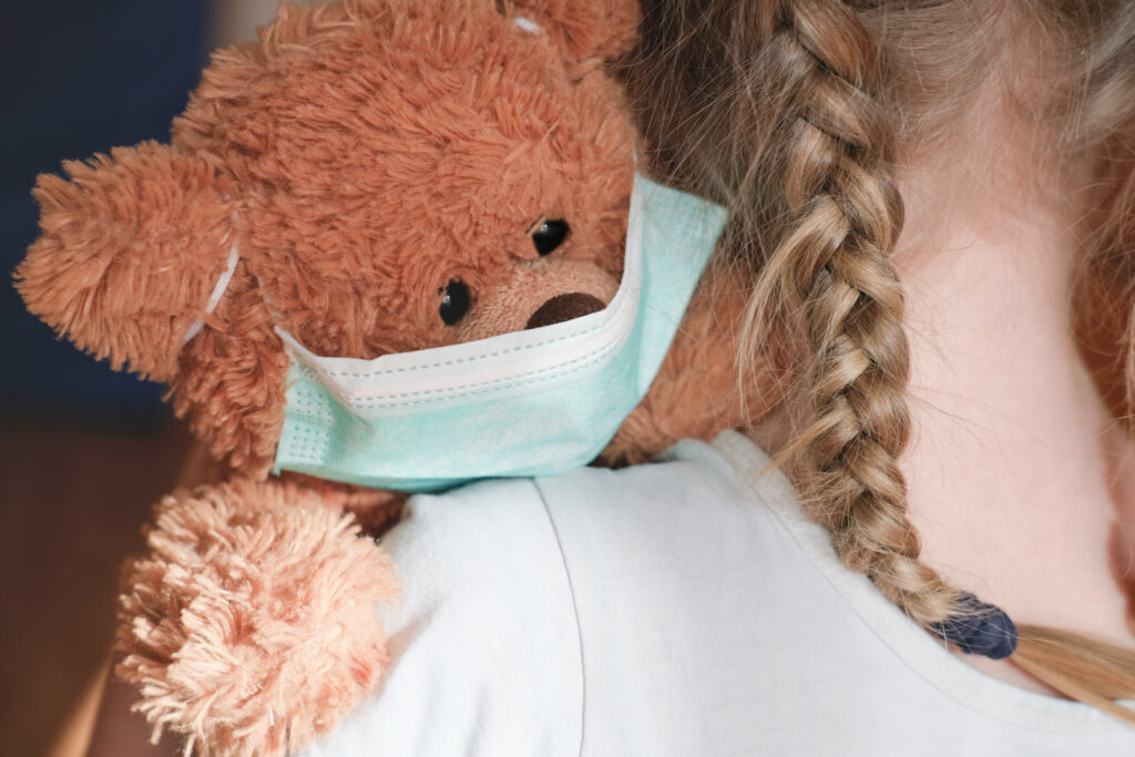 little girl cuddling teddy bear in medical mask to protect from coronavirus. stay at home concept. virus outbreak prevention.